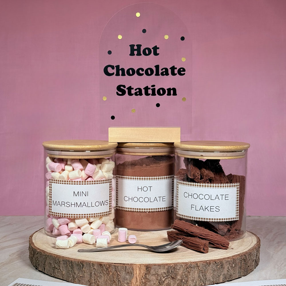 Picture showing three glass jars containing hot chocolate ingredients and a sign that reads hot chocolate station