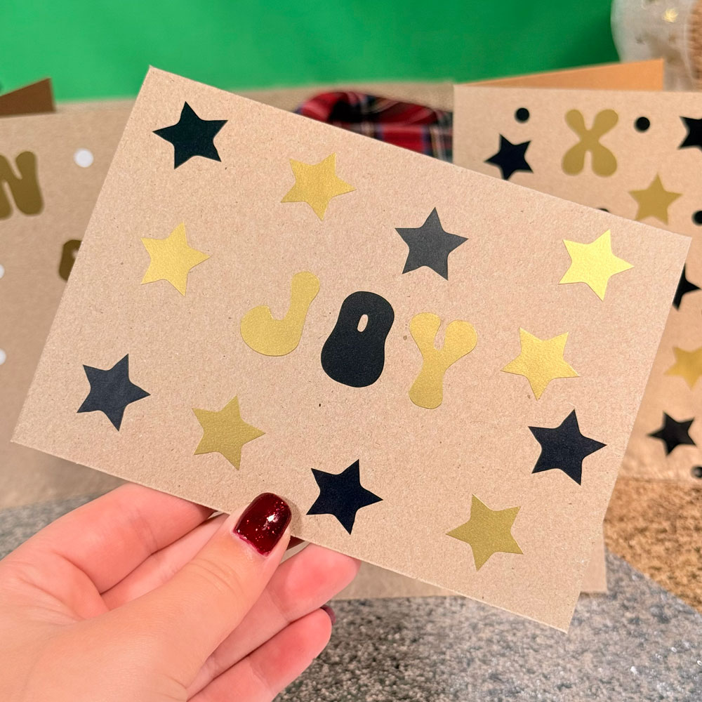 Picture showing a brown greetings card decorated with black and gold stickers spelling out 'JOY' surrounded by stars